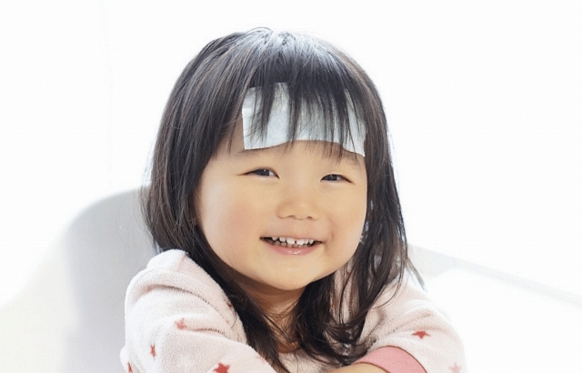 冷却シートでおでこを冷やす笑顔の女の子